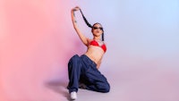 a woman in a red bikini and blue pants is doing a dance on a pink background